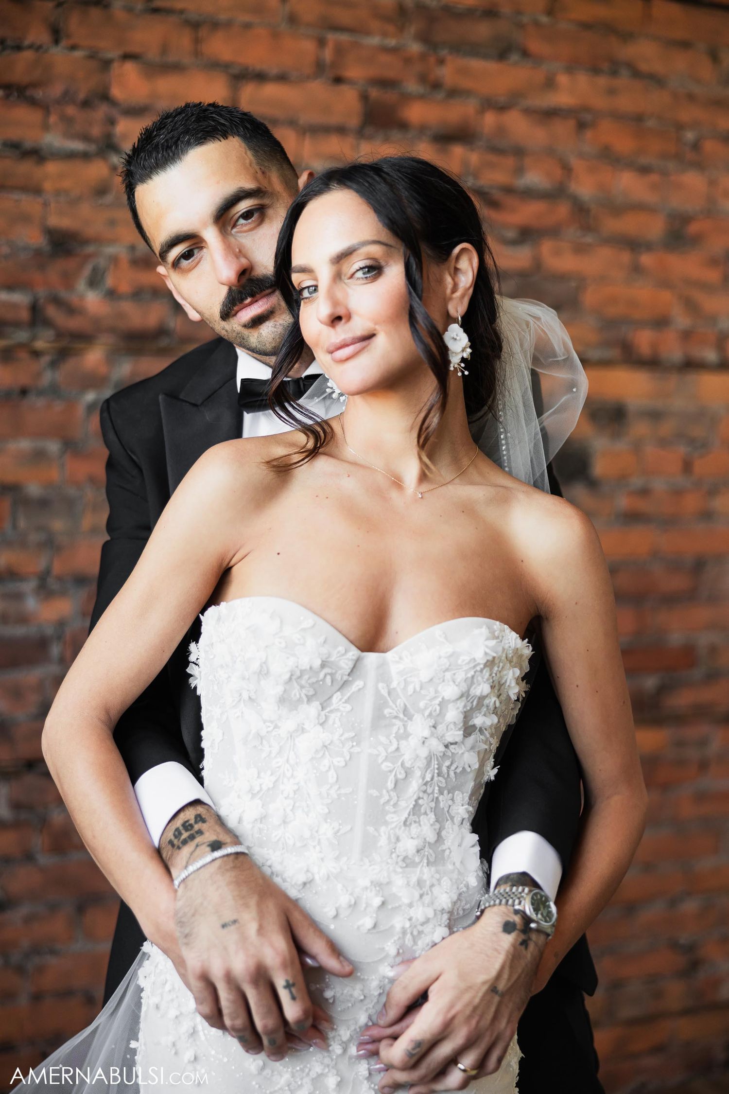 Portrait of newlyweds against rustic brick wall backdrop.