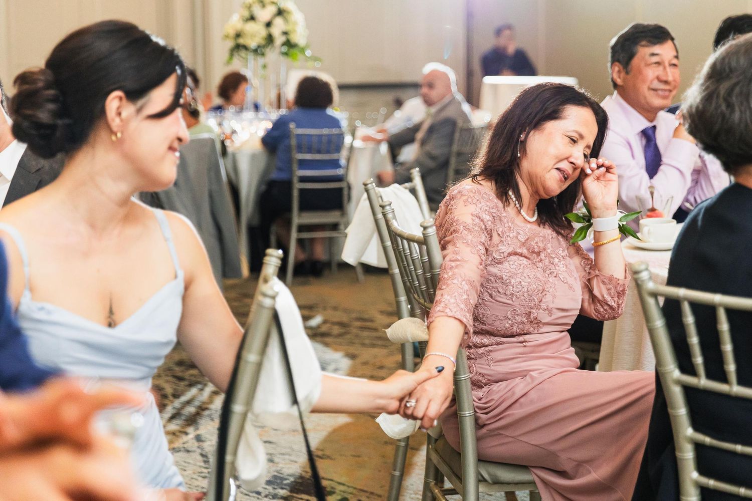 Wedding guests share laughter and conversation at reception tables decorated with floral centerpieces.