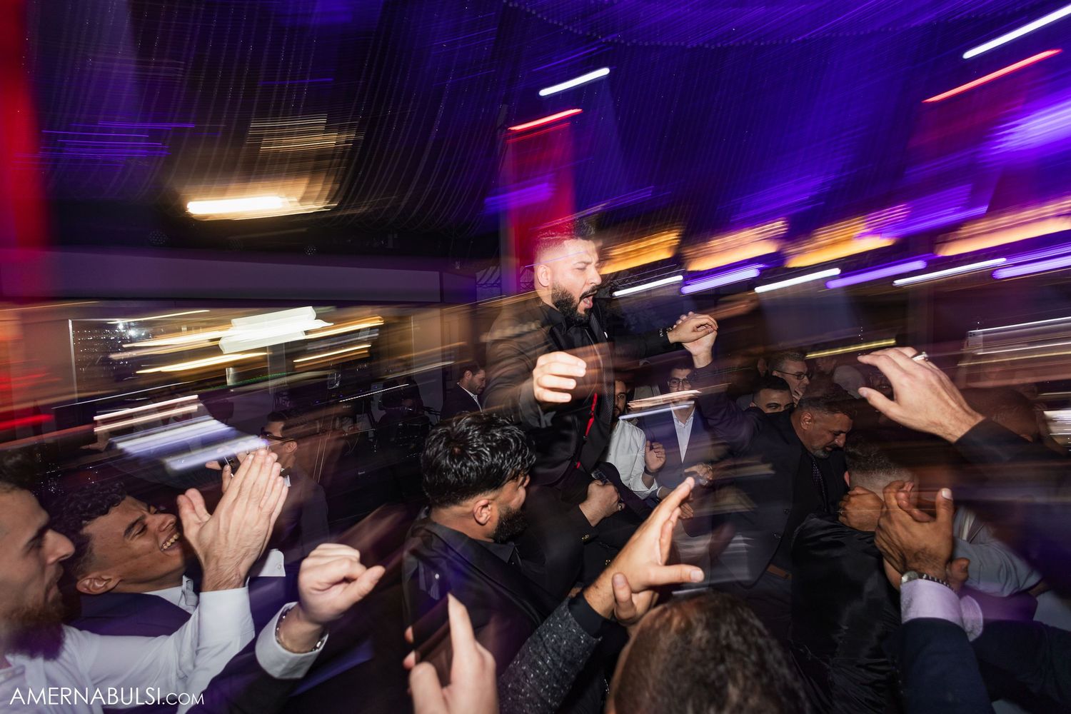 A performer crowd surfs above an energetic audience in a dimly lit venue with purple lighting effects.