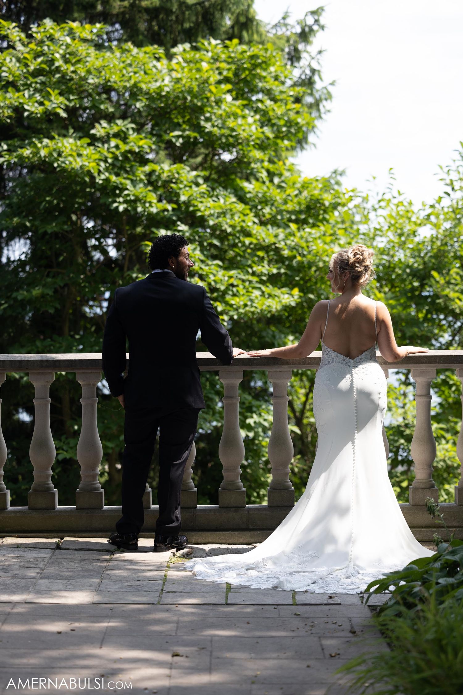 Couple shares quiet moment overlooking garden from stone balcony in wedding attire.