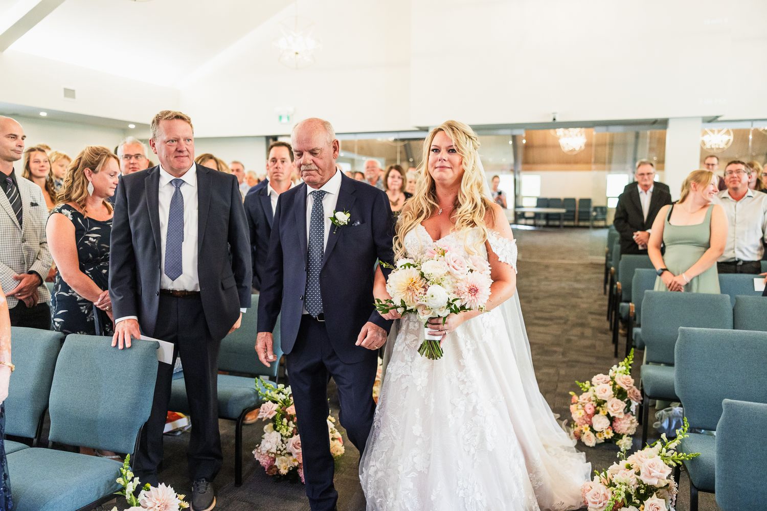 Wedding ceremony in progress inside a modern church with blue chairs and natural lighting.