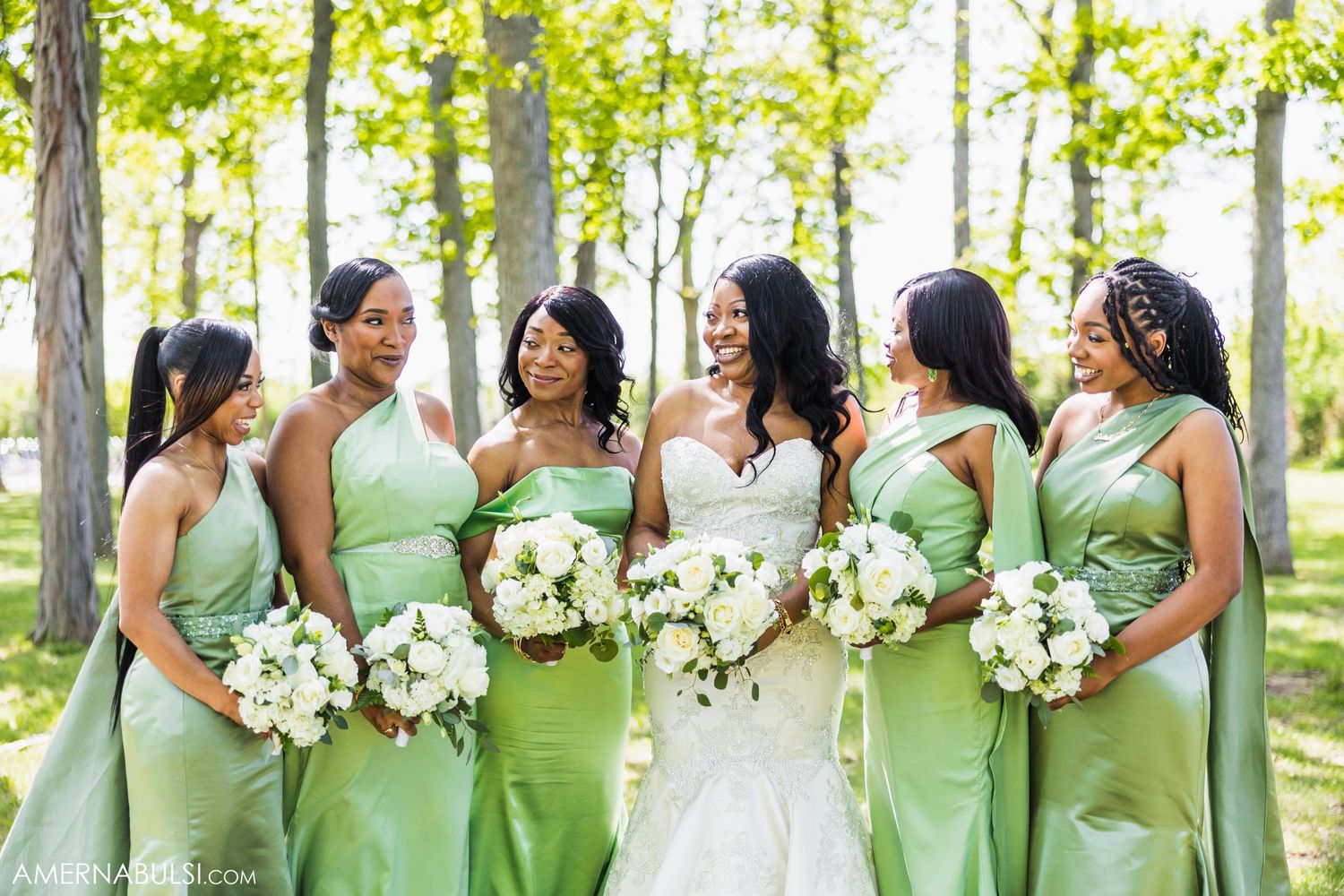 Bridesmaids in mint green dresses holding white bouquets pose with bride in outdoor garden setting.
