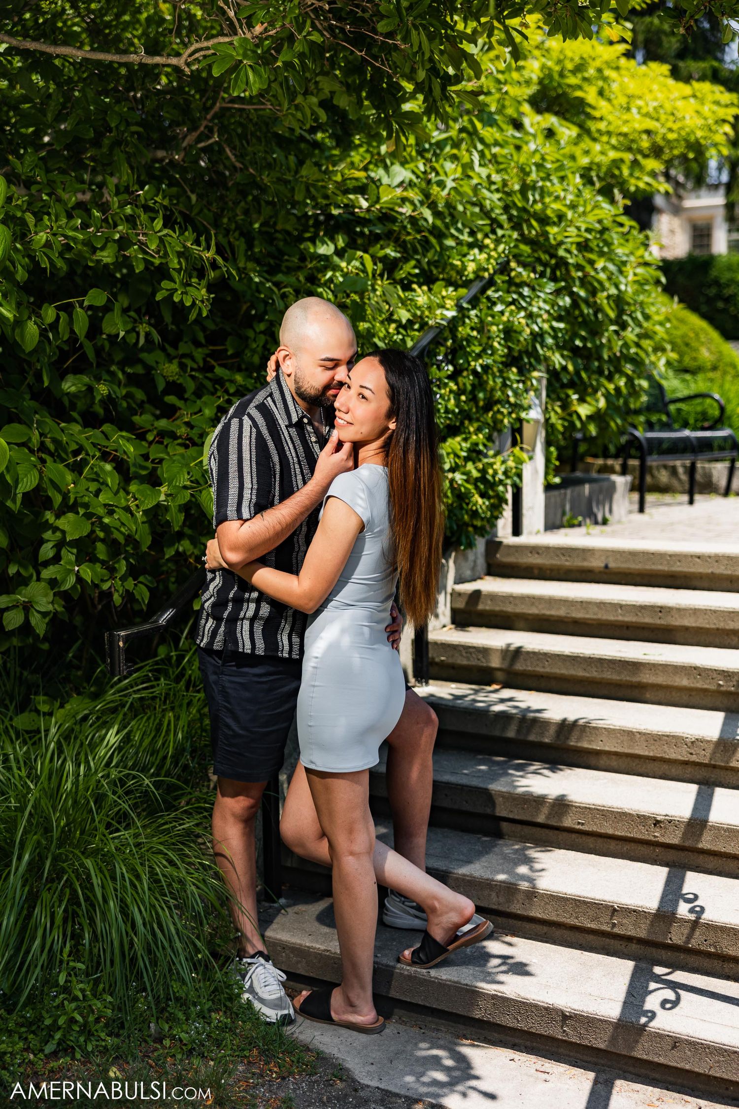 Romantic couple embracing on stone steps surrounded by lush summer greenery.