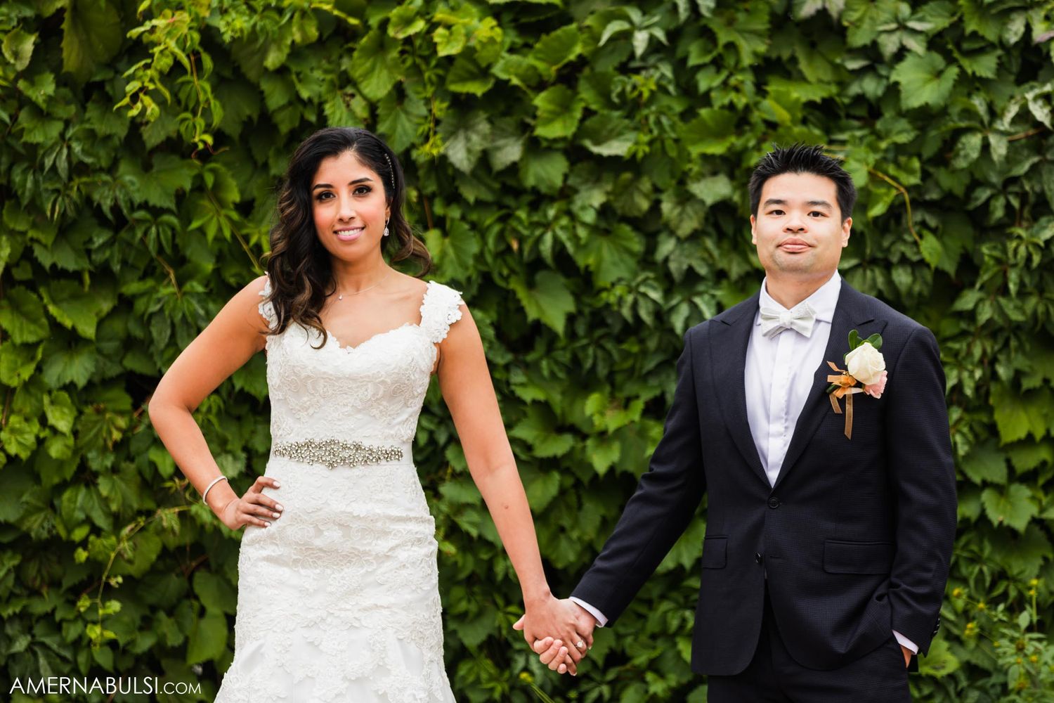A couple poses against a leafy green wall backdrop during their wedding portraits.