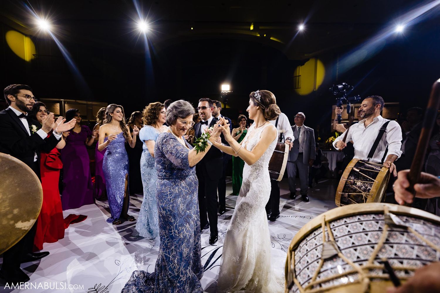 Wedding party dances and celebrates with live music on a brightly lit dance floor.