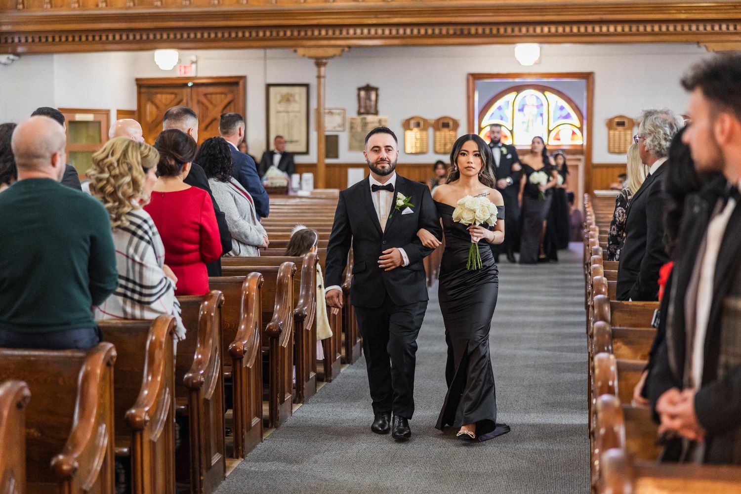 Wedding processional moves through traditional church with wooden pews and decorative details.
