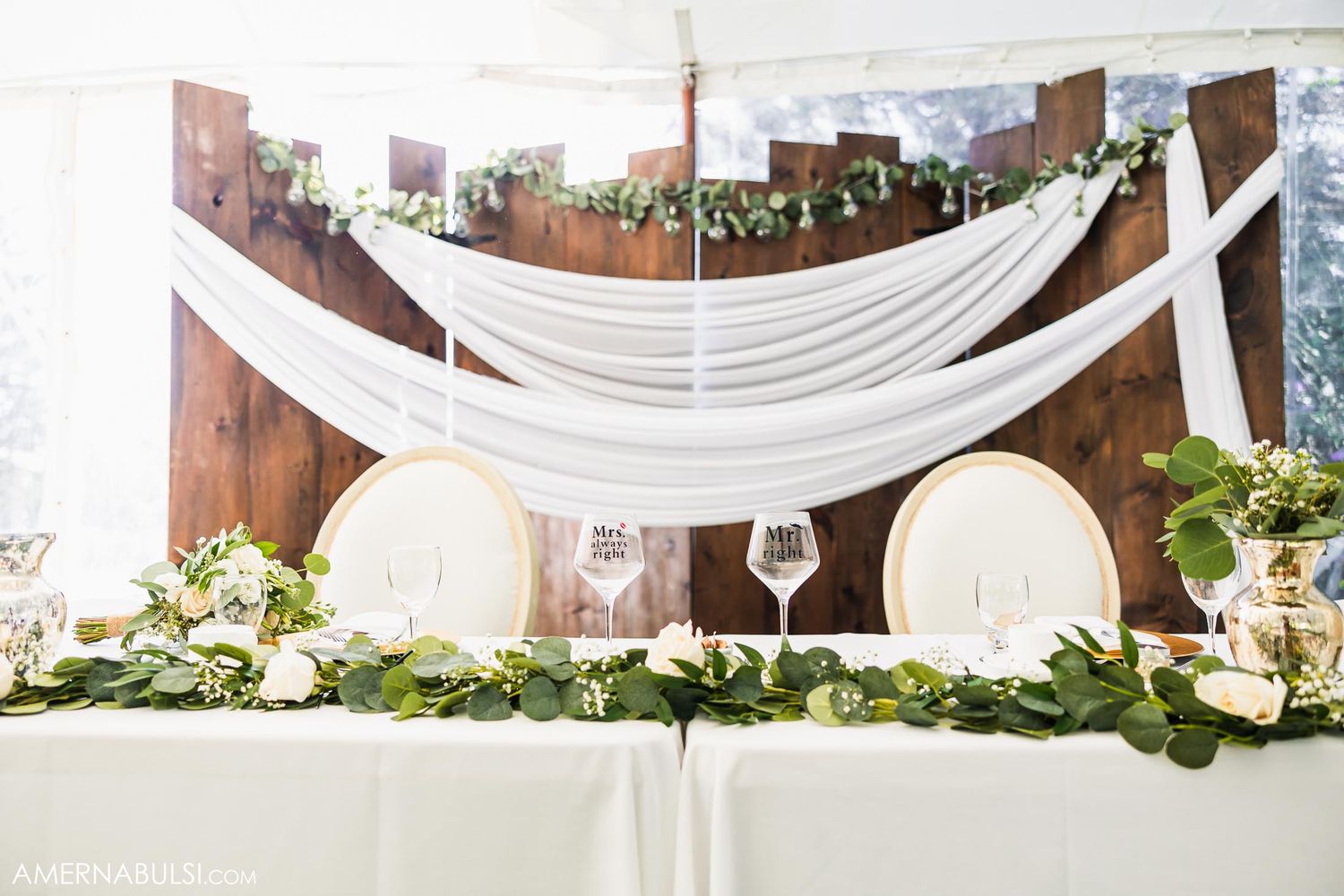 White draped fabric and lantern decorations adorn an elegant wedding reception head table.