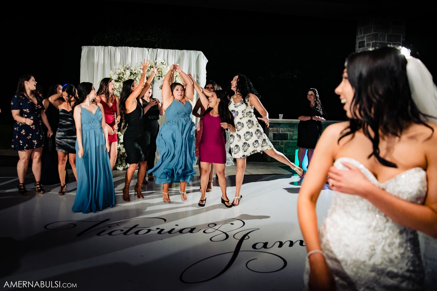 Wedding party guests dance and celebrate on a dimly lit dance floor during an evening reception celebration.