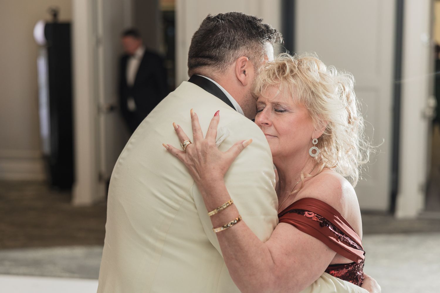 Couple sharing an intimate slow dance embrace at a formal event, woman in red dress, man in cream suit.