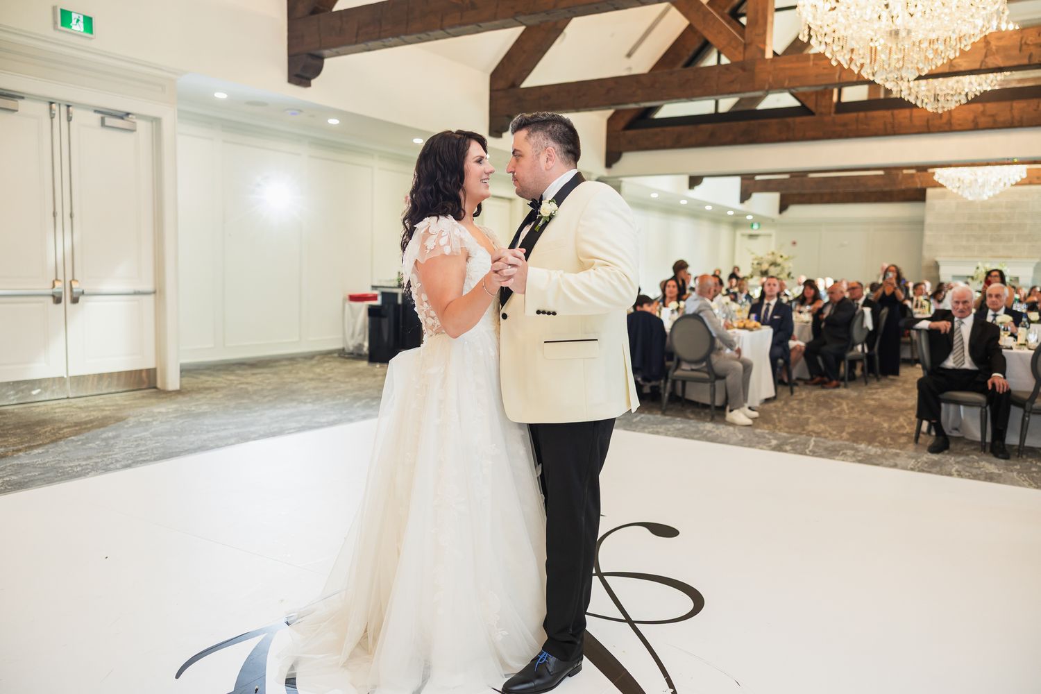 Bride and groom share their first dance on a white dance floor at an elegant wedding reception venue.