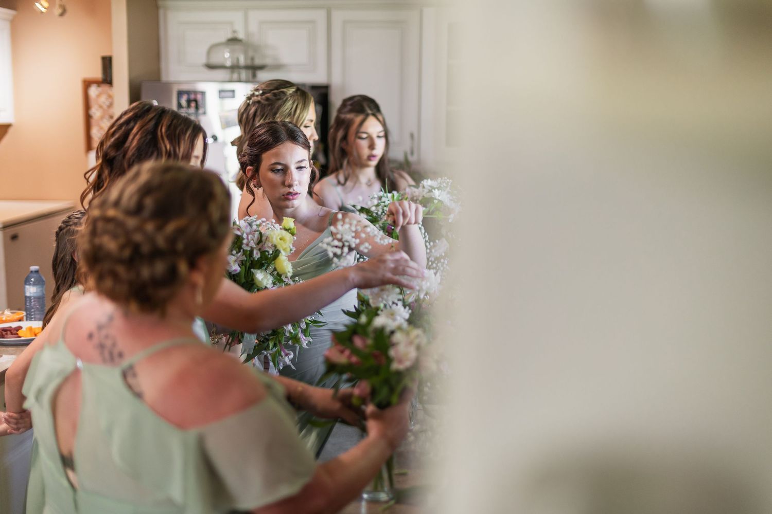 Bridesmaids in mint green dresses arranging white floral bouquets together indoors before a wedding ceremony.