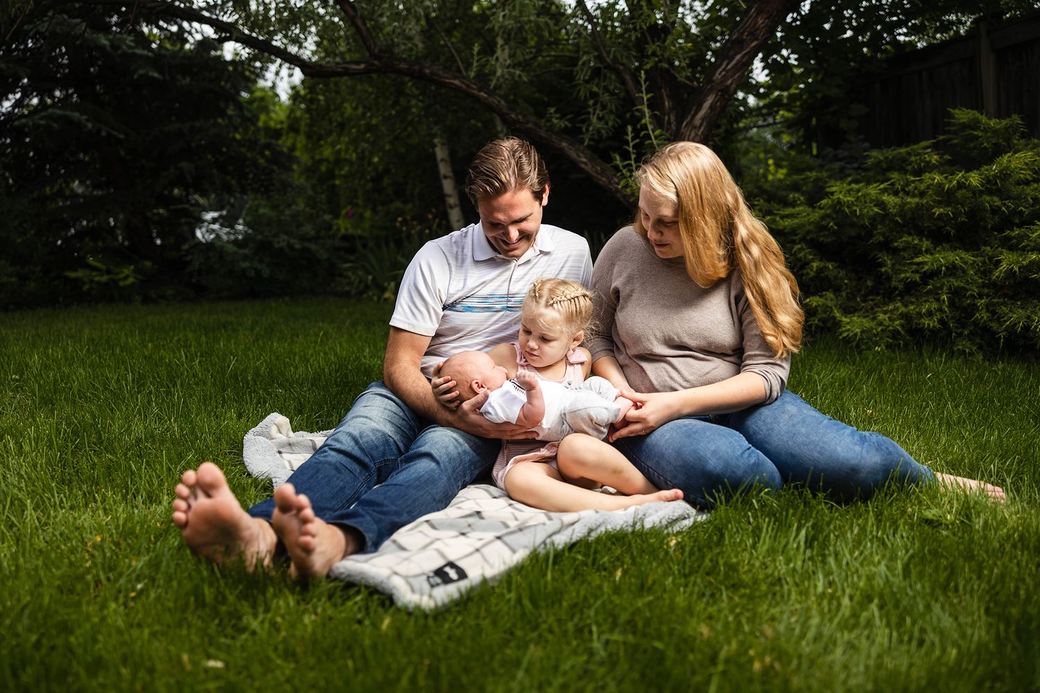 Family relaxing together on a picnic blanket in a lush green field on a sunny summer day.