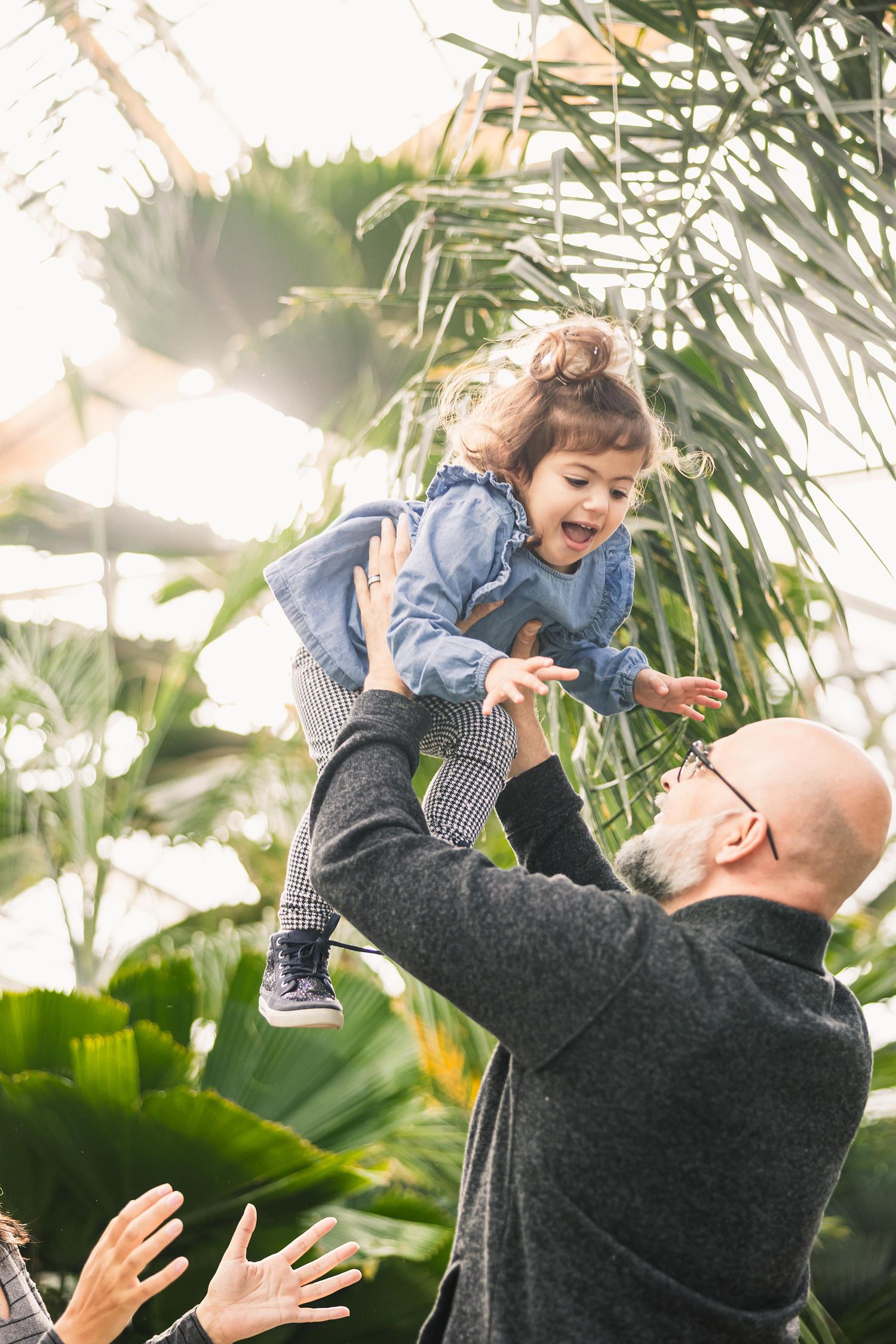 Playful moment captured as parent tosses laughing child in the air surrounded by tropical plants.