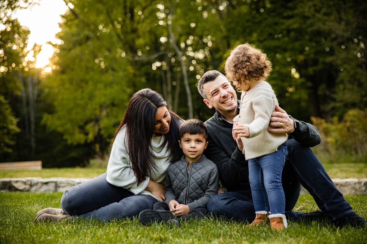 Family lying together on grass in park during autumn sunset photoshoot.