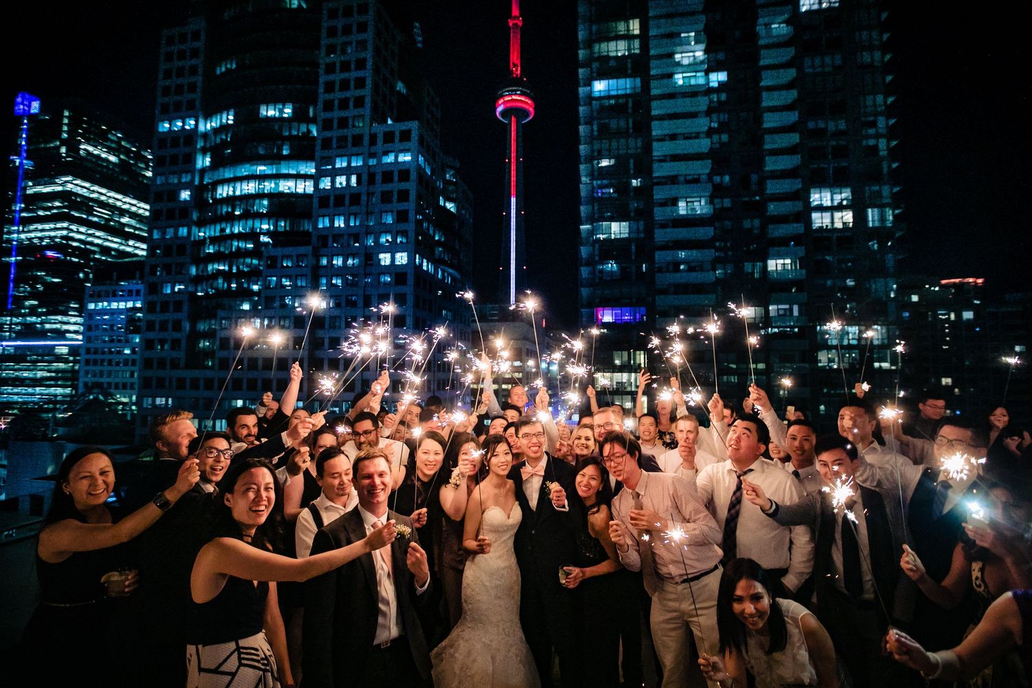 Nighttime wedding celebration with Toronto skyline and CN Tower illuminated in background.