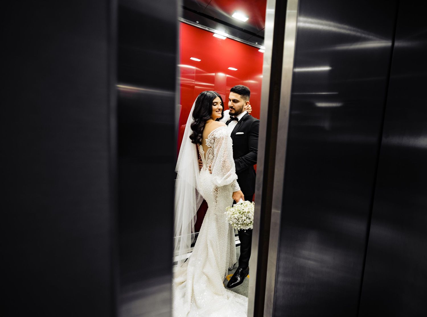 Wedding couple enters through dramatic red-lit elevator doors.