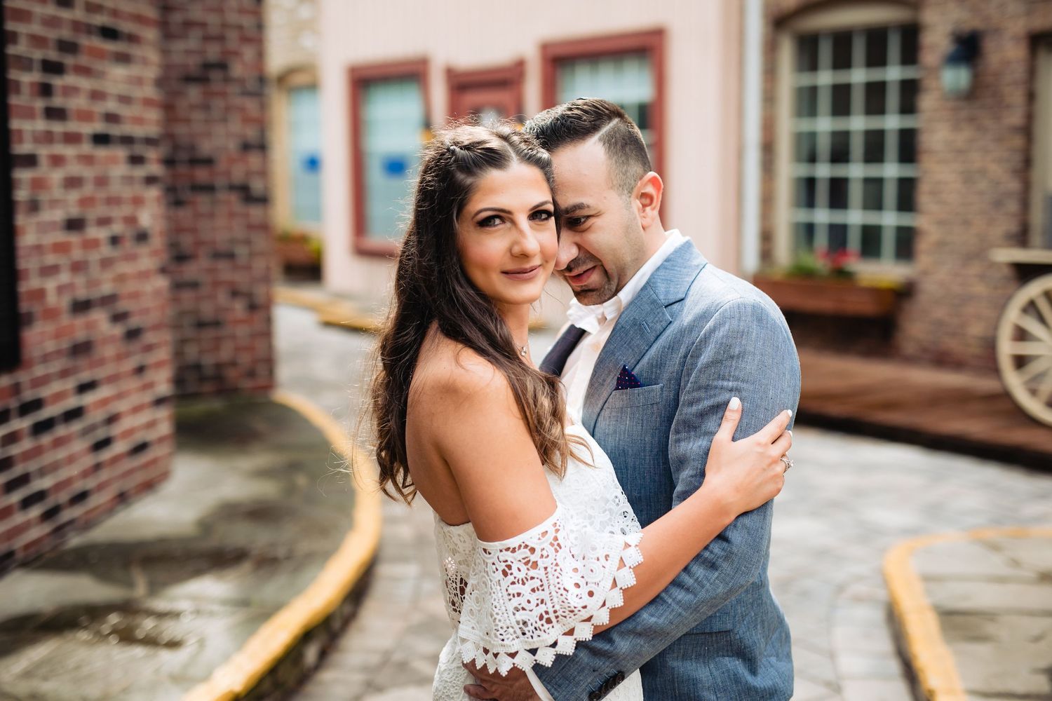 A couple poses together against a brick building with classic architecture.