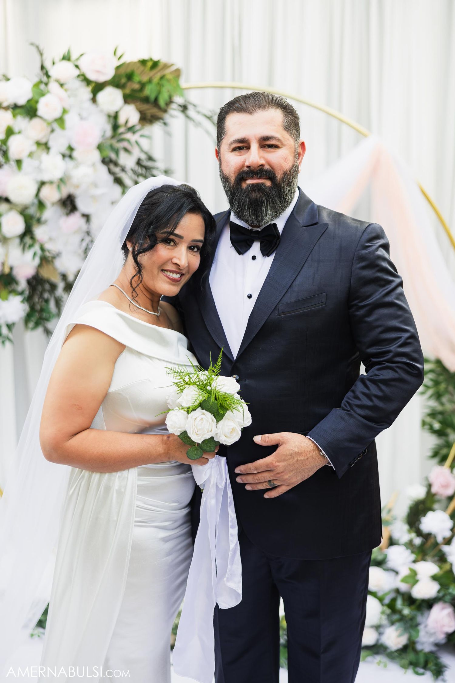 Classic formal wedding portrait with floral arch backdrop.