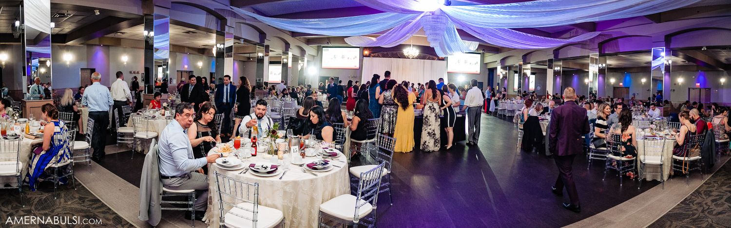 Wide angle view of an elegant wedding reception space with purple uplighting and draped ceiling decor.