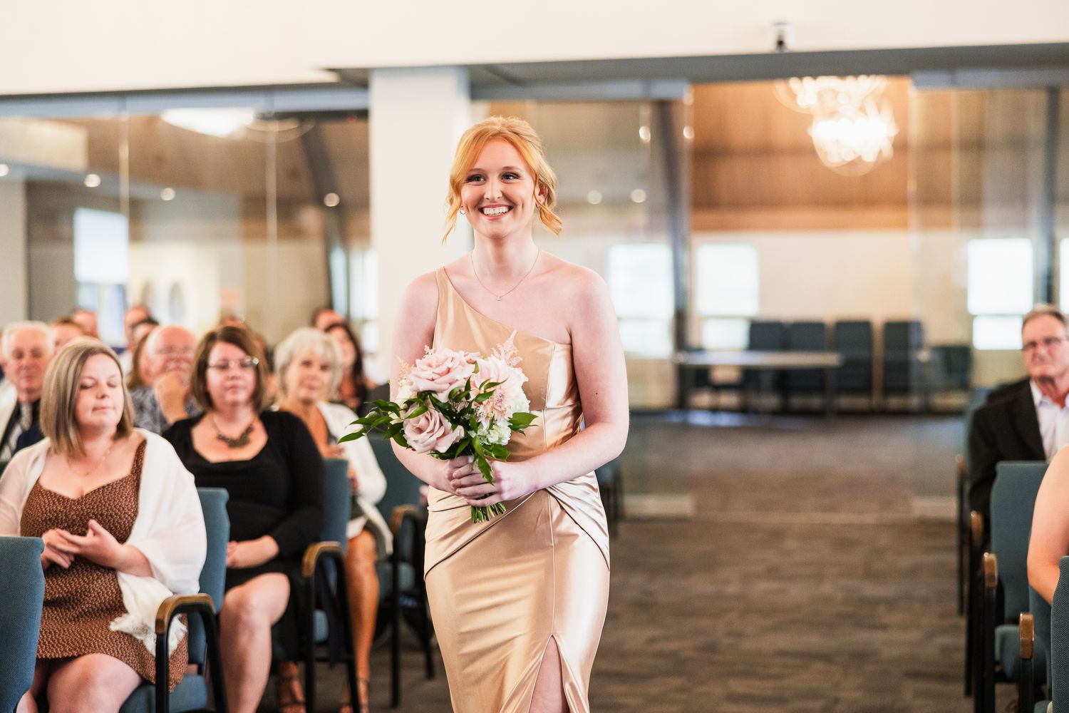 Wedding ceremony setup in elegant indoor venue with guests seated in rows and chandeliers overhead.