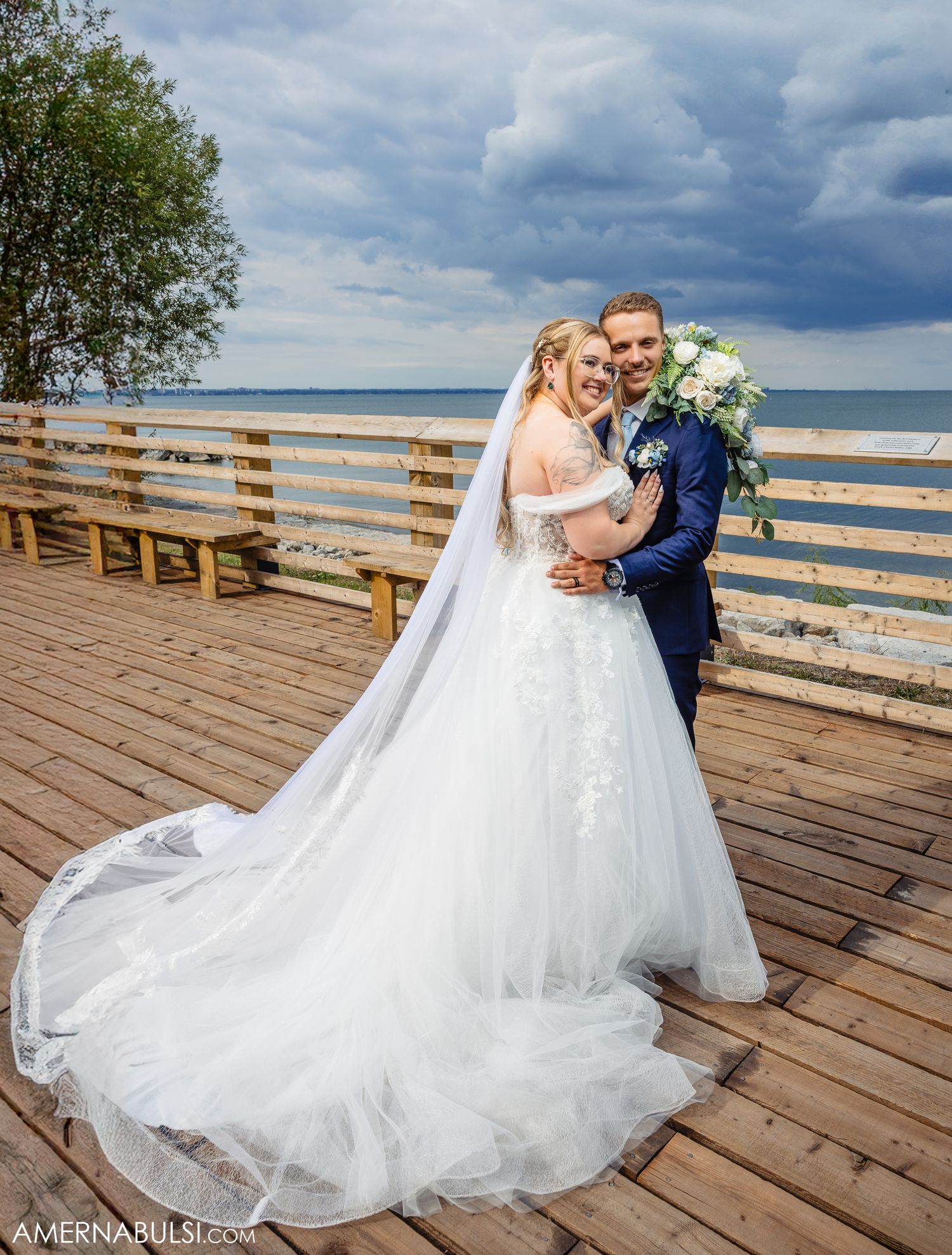 Couple shares romantic moments on a wooden pier overlooking a scenic beachfront under dramatic cloudy skies.