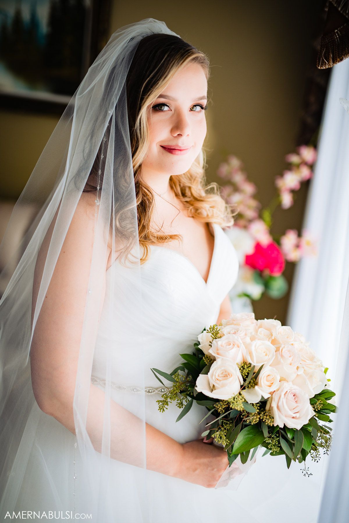 A bride in a white wedding dress holds a bouquet of pale pink roses.