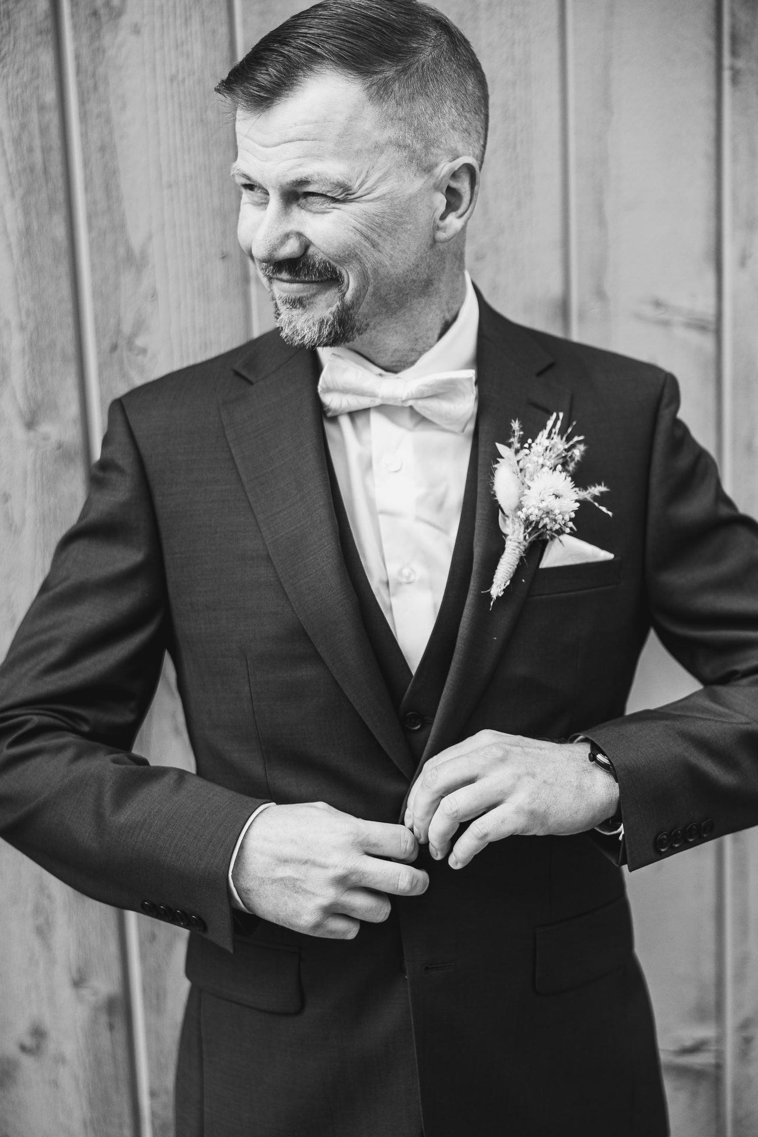 Black and white portrait of suited person smiling while adjusting attire.
