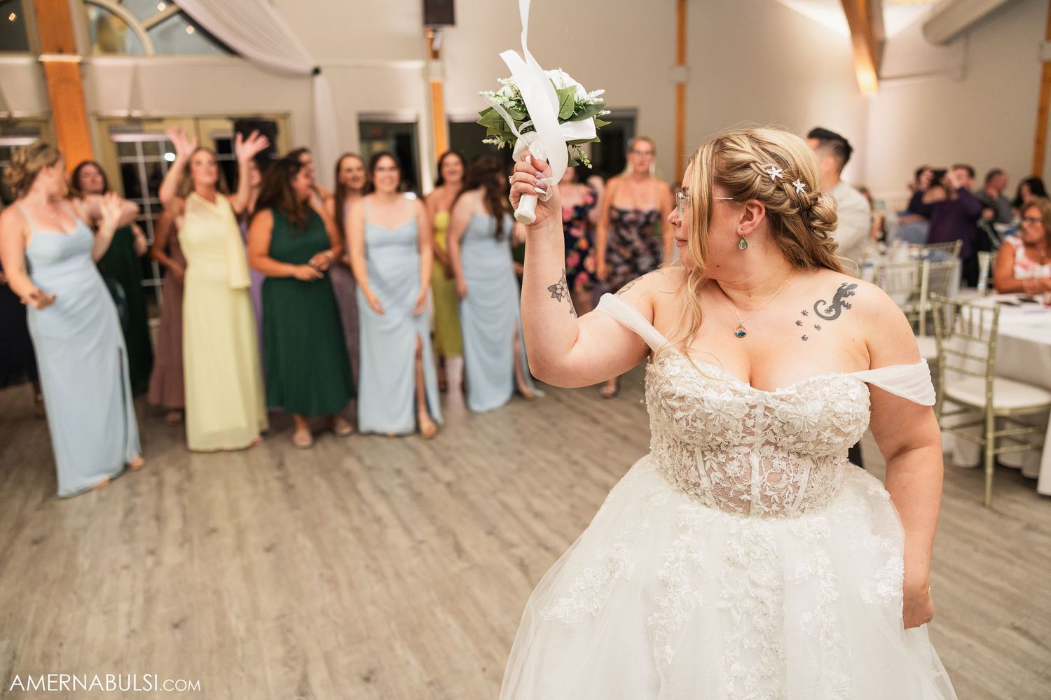 Wedding celebration with guests dancing and celebrating in an elegant reception hall with wood floors.