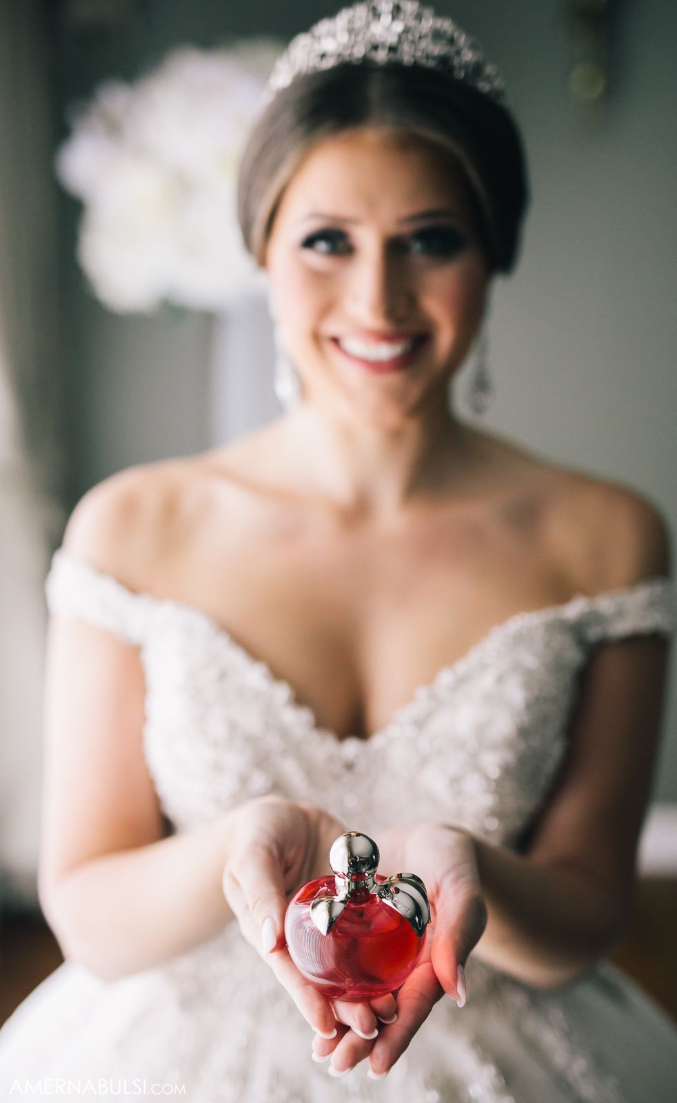 Close-up of a perfume bottle being held against a white wedding dress.