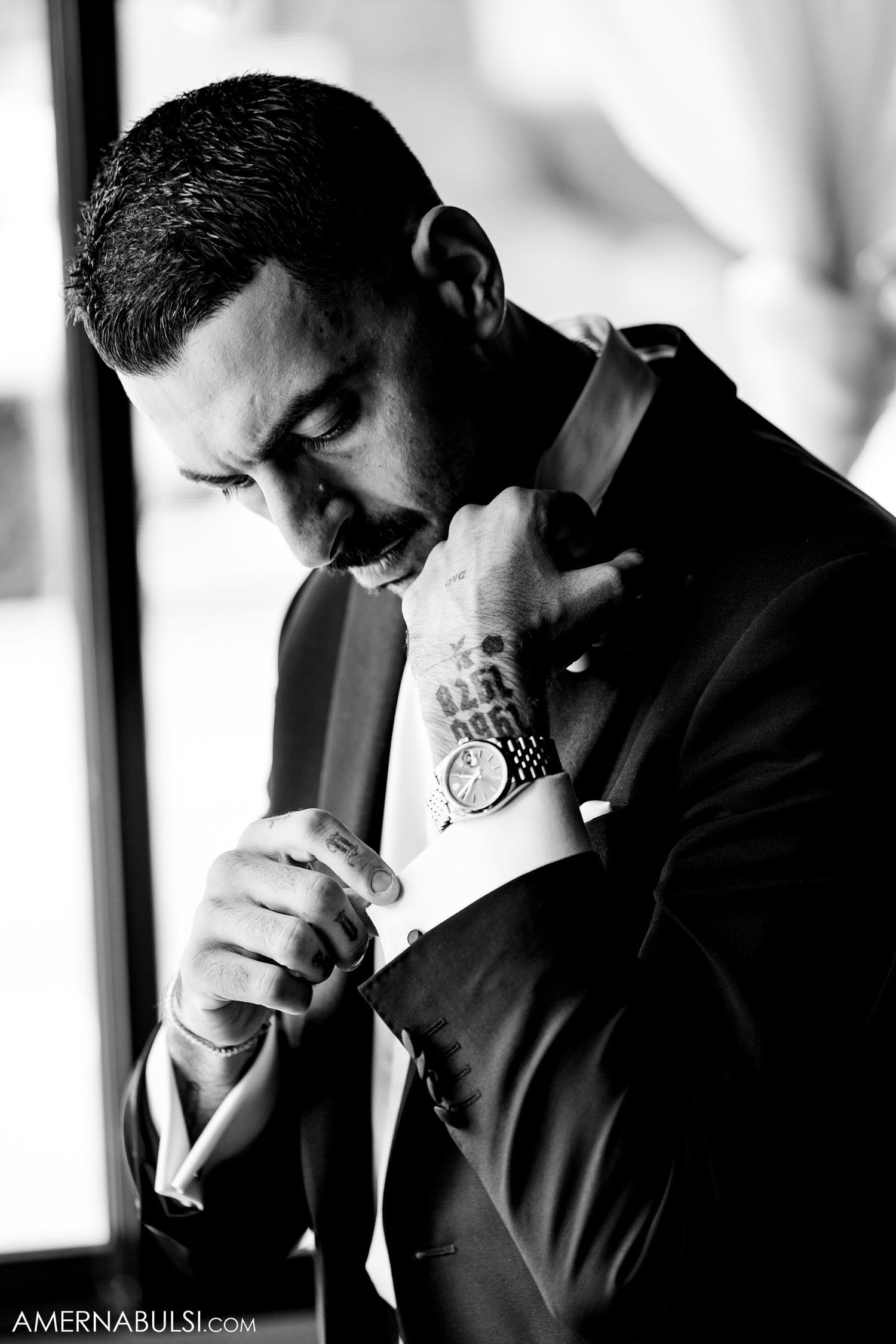 Black and white portrait of someone adjusting their bowtie in dramatic lighting.
