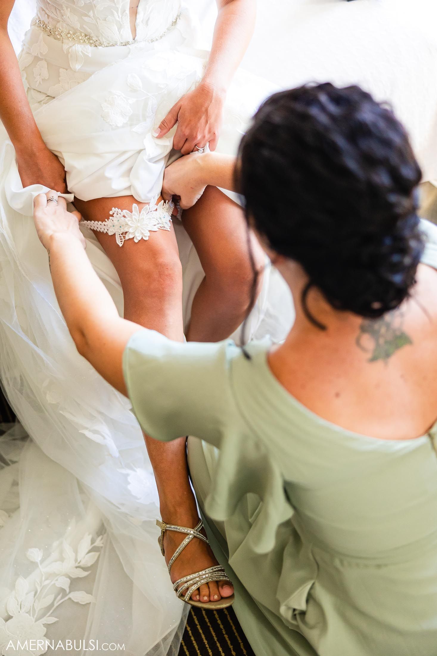 A lace wedding garter being placed on a bride's leg with silver strappy sandals.