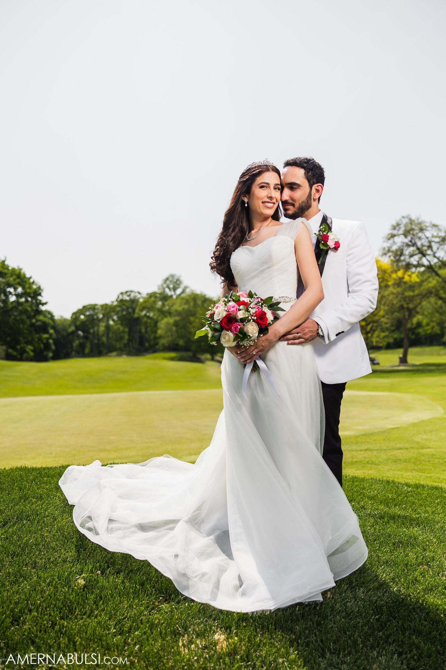 Elegant wedding couple poses with bouquet on golf course green with flowing white dress.