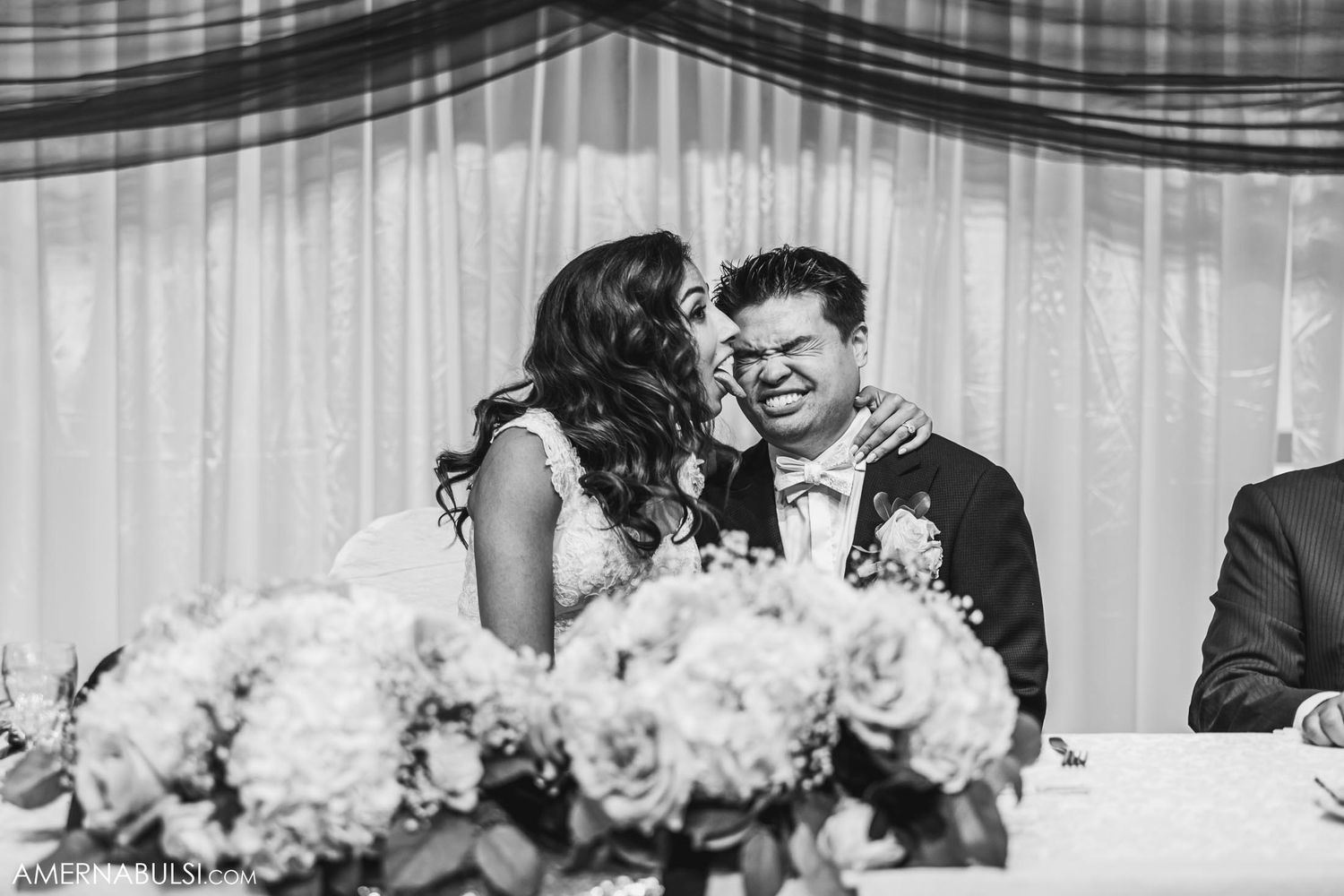 Black and white candid moment of couple at wedding reception with floral centerpiece.