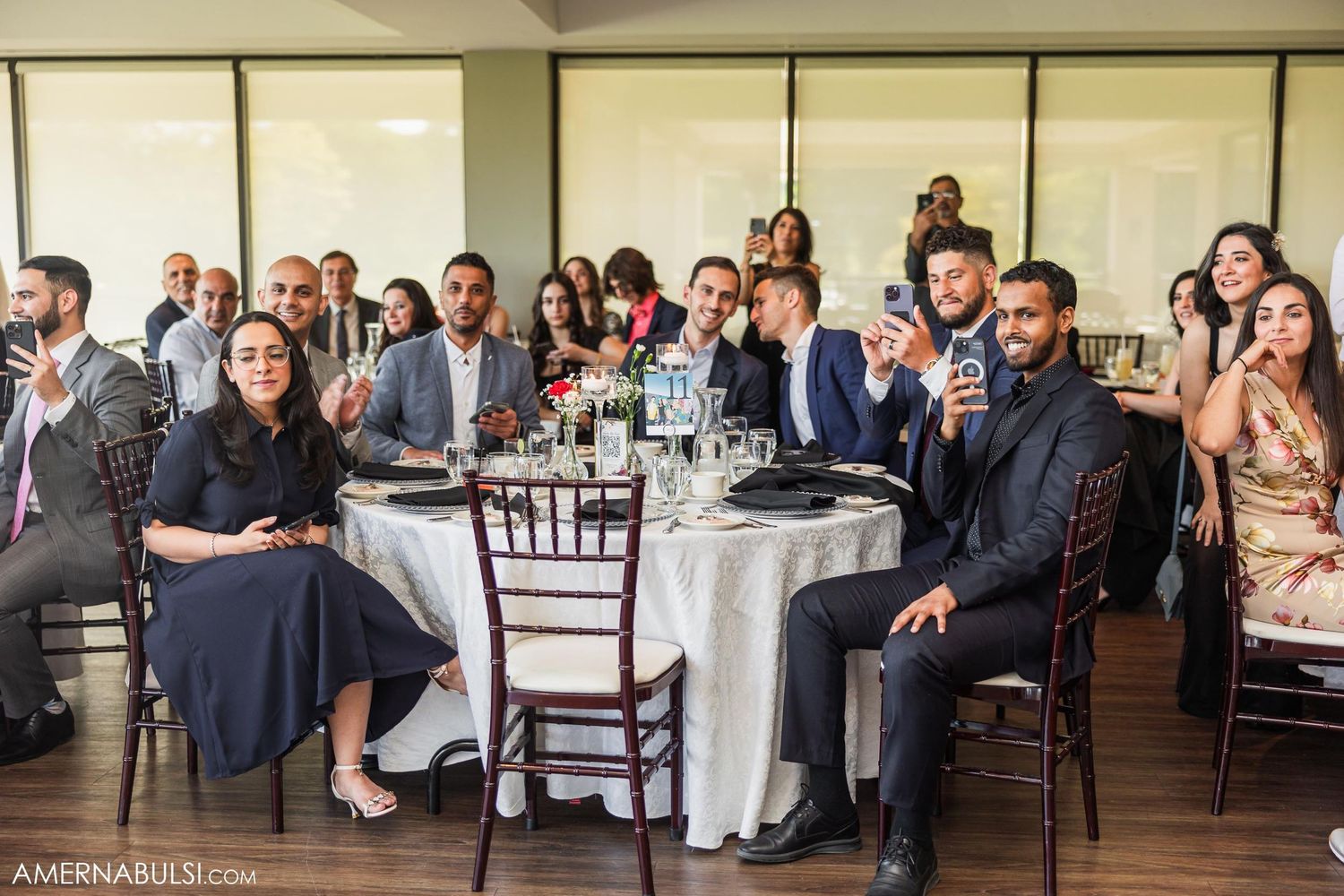 Wedding reception guests seated at formal round tables with elegant place settings and decor.