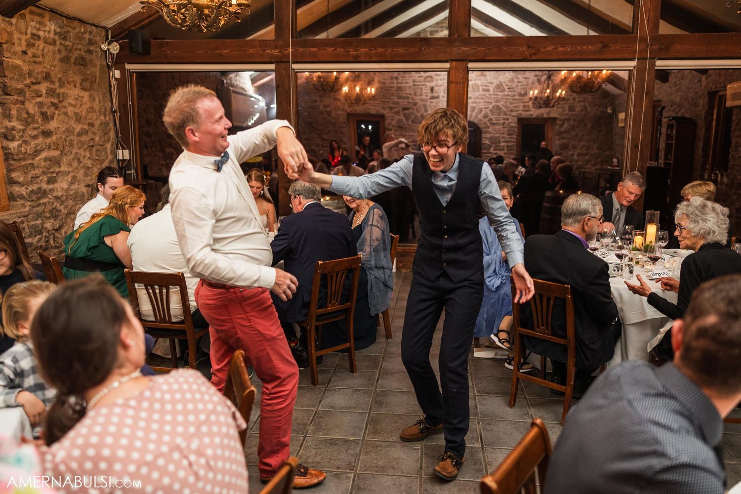 Wedding guests dancing enthusiastically in rustic venue with exposed stone walls.