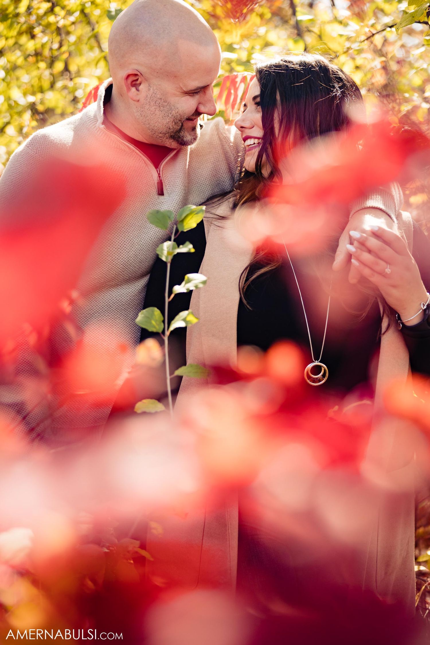 Romantic moment captured through vibrant red fall leaves in foreground.