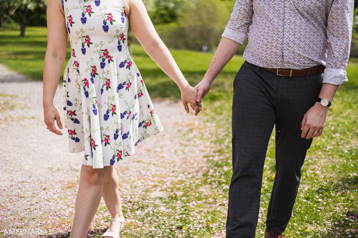 A couple holds hands while walking on a path, wearing coordinated spring outfits.