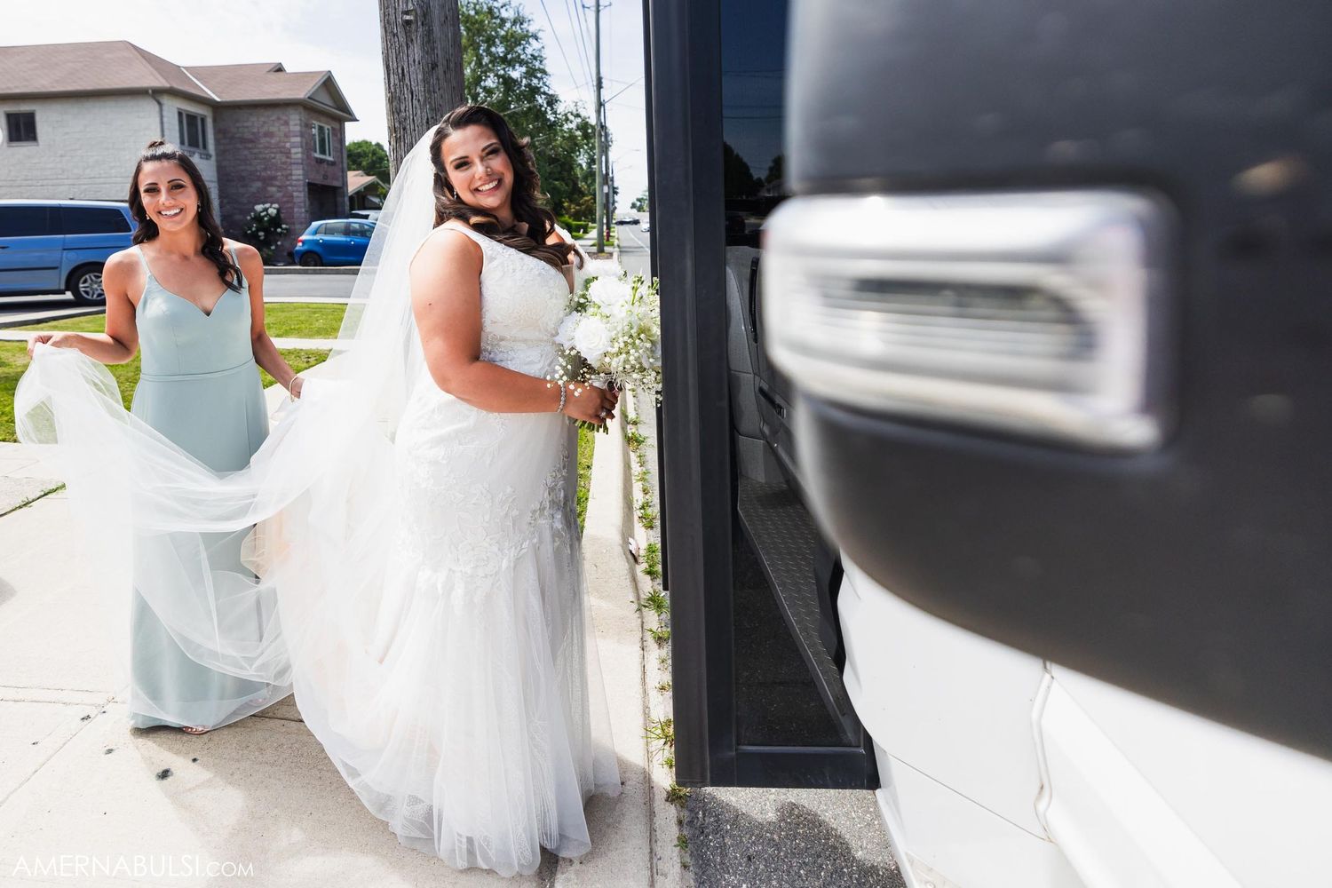 Two people in formal dresses walk outside near a parked vehicle.