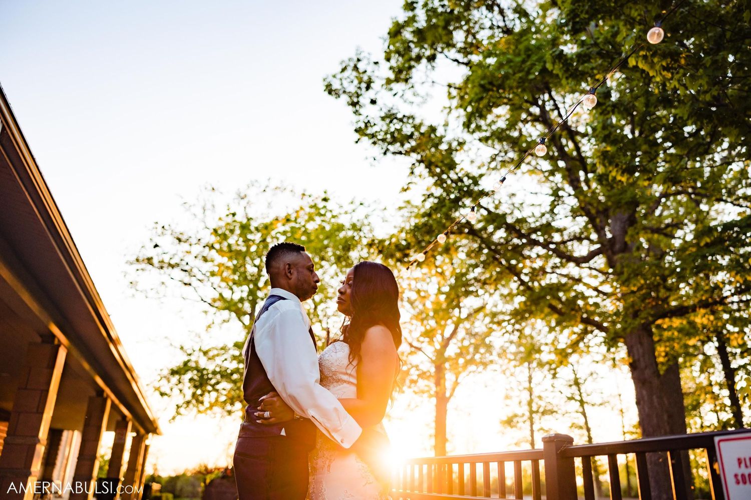 Newlyweds share an intimate moment on a deck during golden hour sunset.