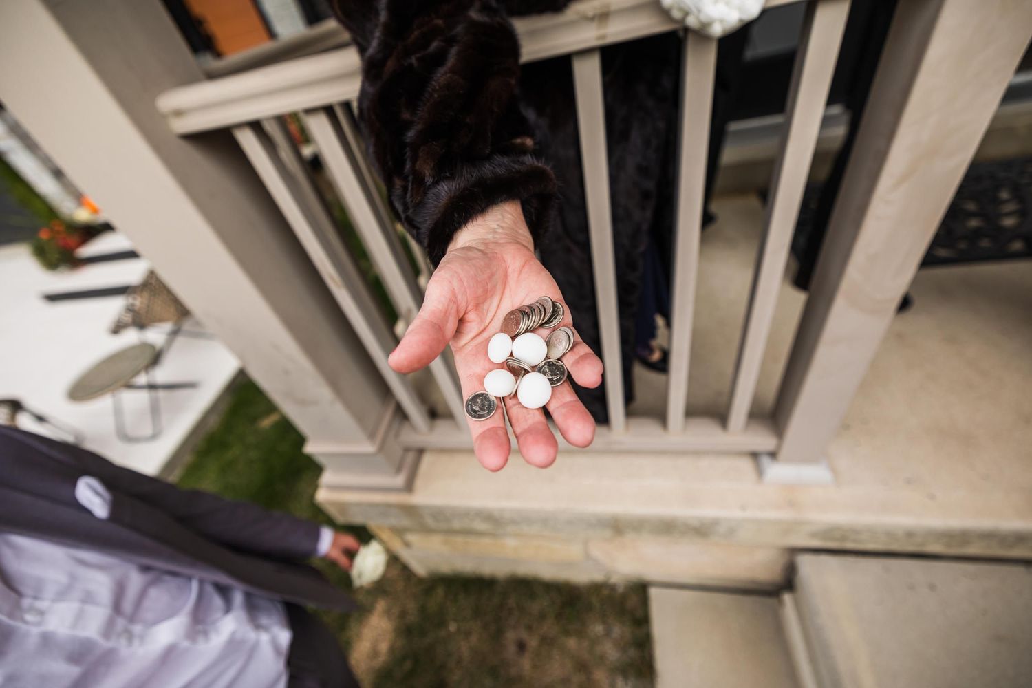 A hand holds wedding rings against white wooden railing posts outdoors.