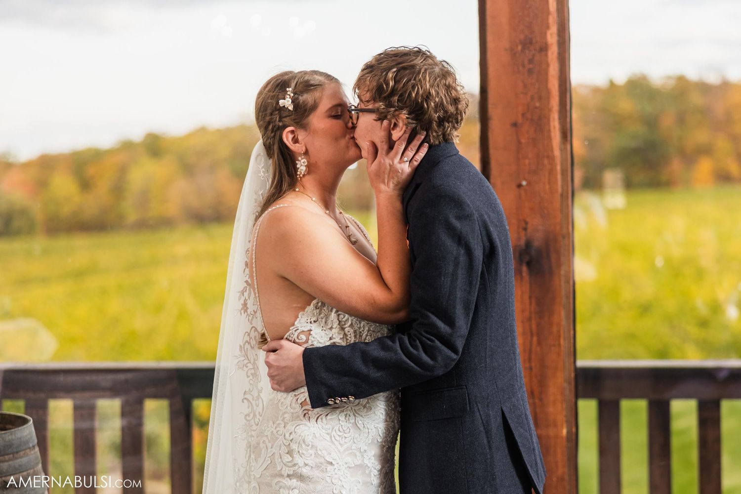 Romantic kiss on outdoor deck with fall foliage backdrop.