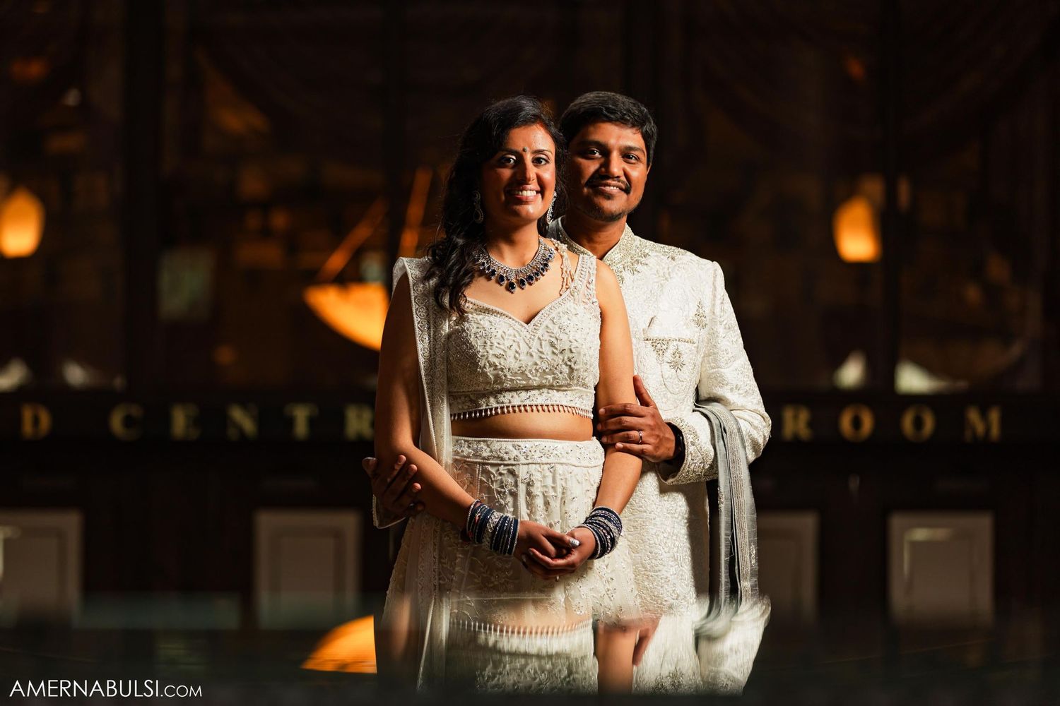 A romantic indoor wedding portrait illuminated by warm lighting and elegant decor.