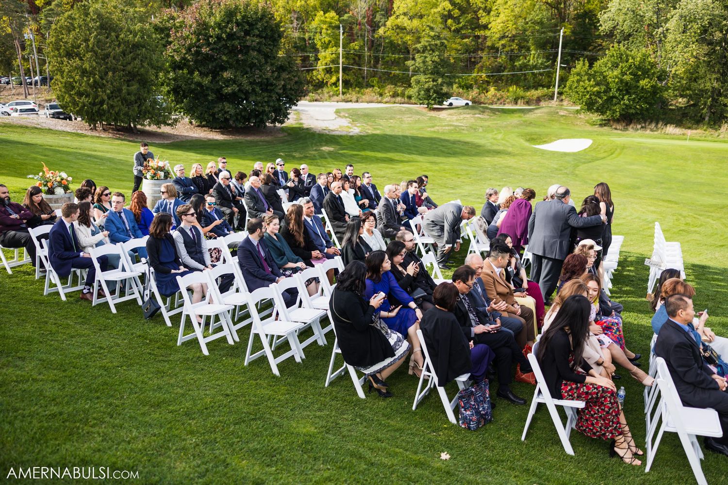 Wedding guests seated in white chairs on manicured lawn for outdoor ceremony.