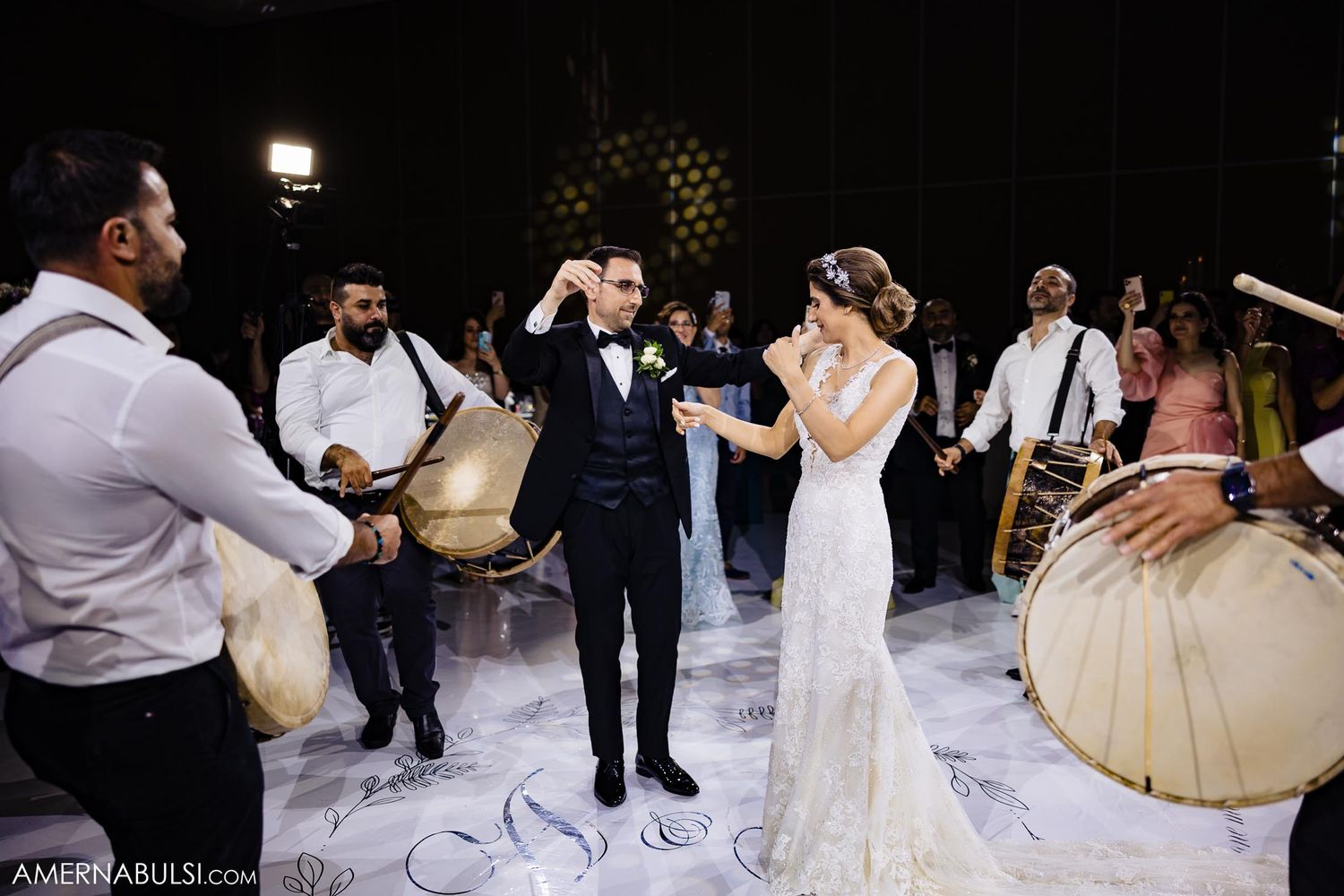 Drummers create a lively atmosphere while newlyweds dance on a white floor during reception celebrations.