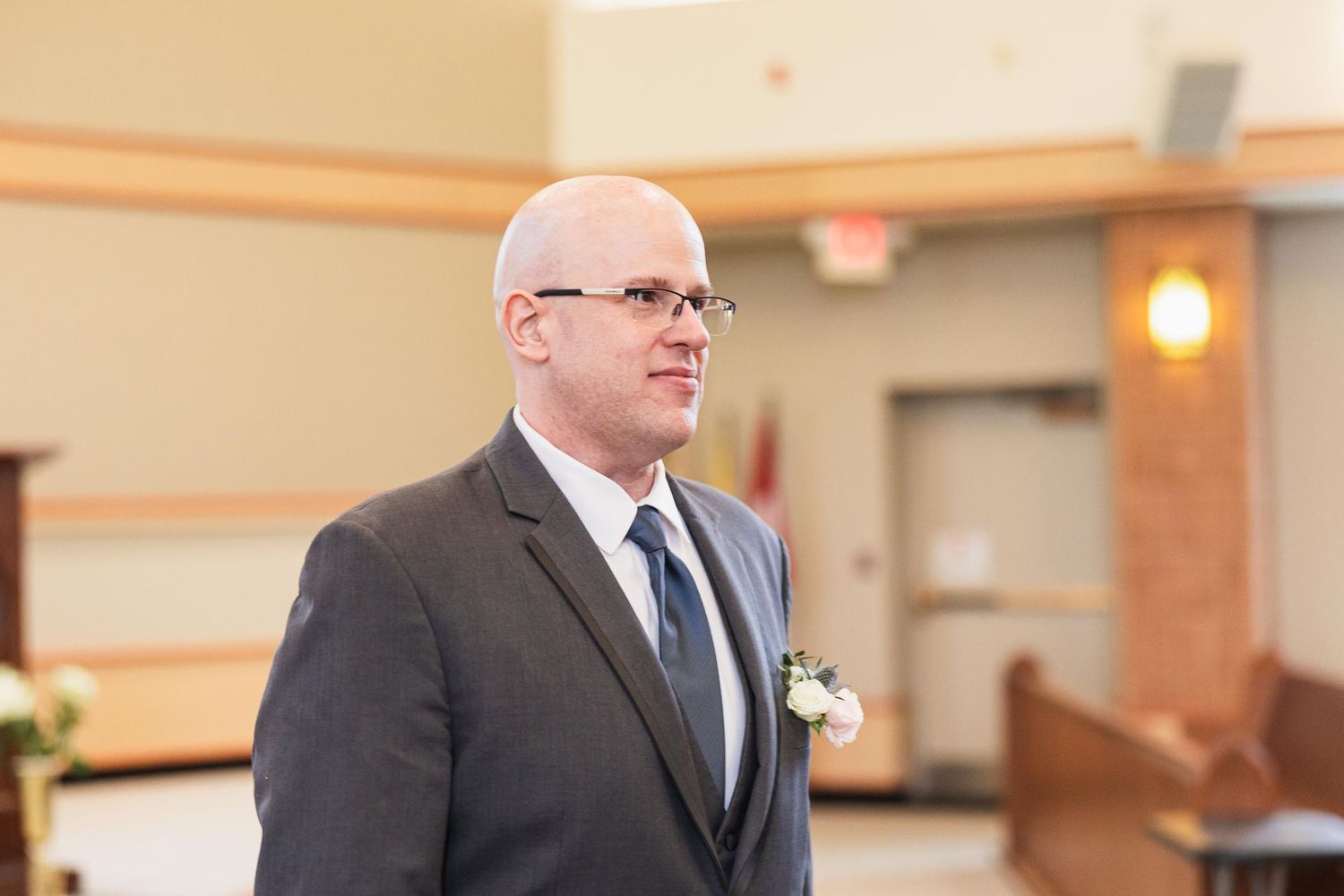 A person in a grey suit and tie stands at the altar during a wedding ceremony.