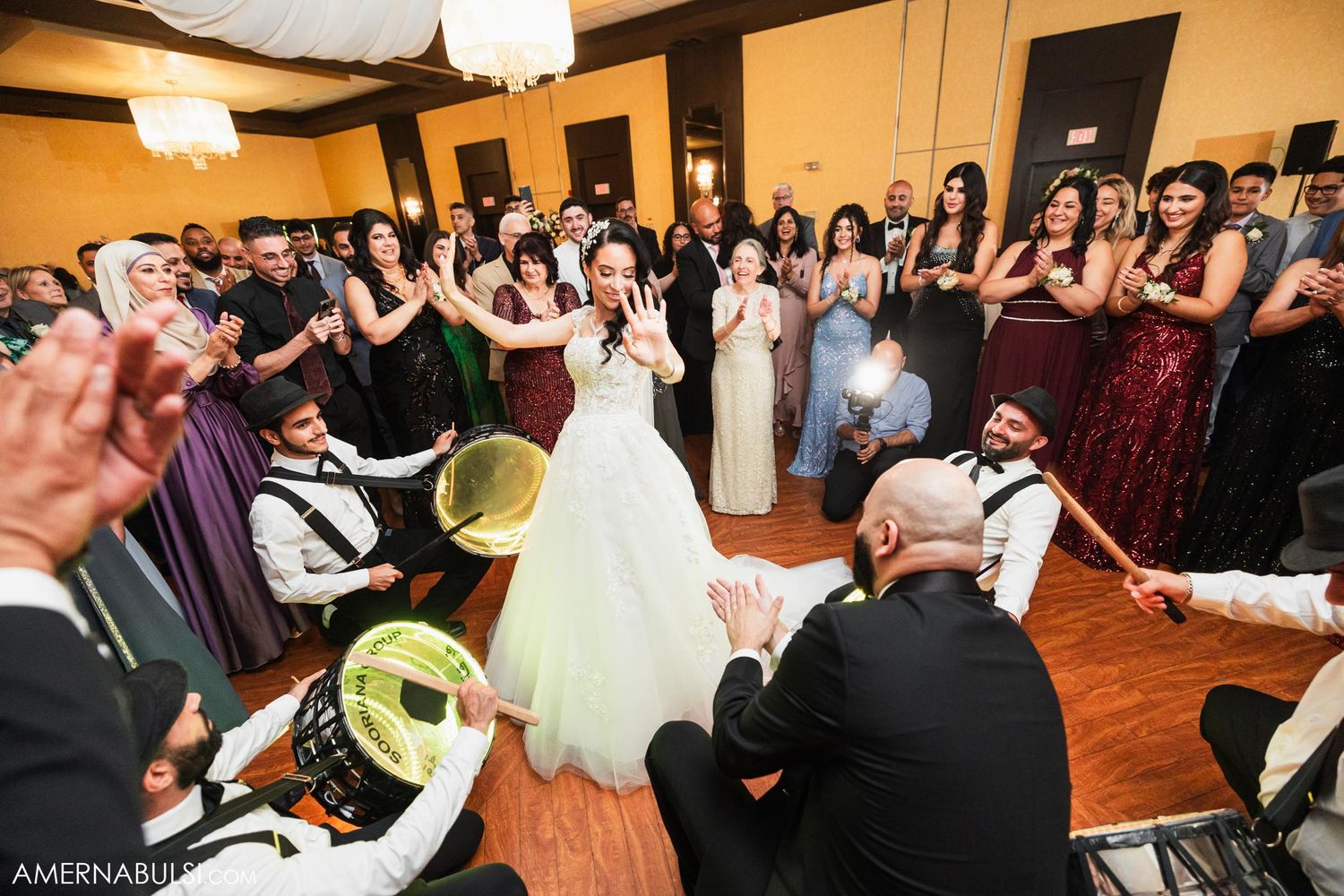 Wedding guests gather around musicians performing with traditional instruments on a wooden dance floor.