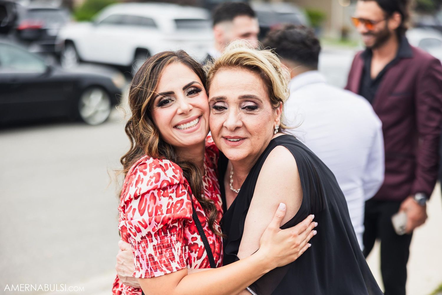 Two wedding guests embrace and smile while celebrating outside during daytime celebration.