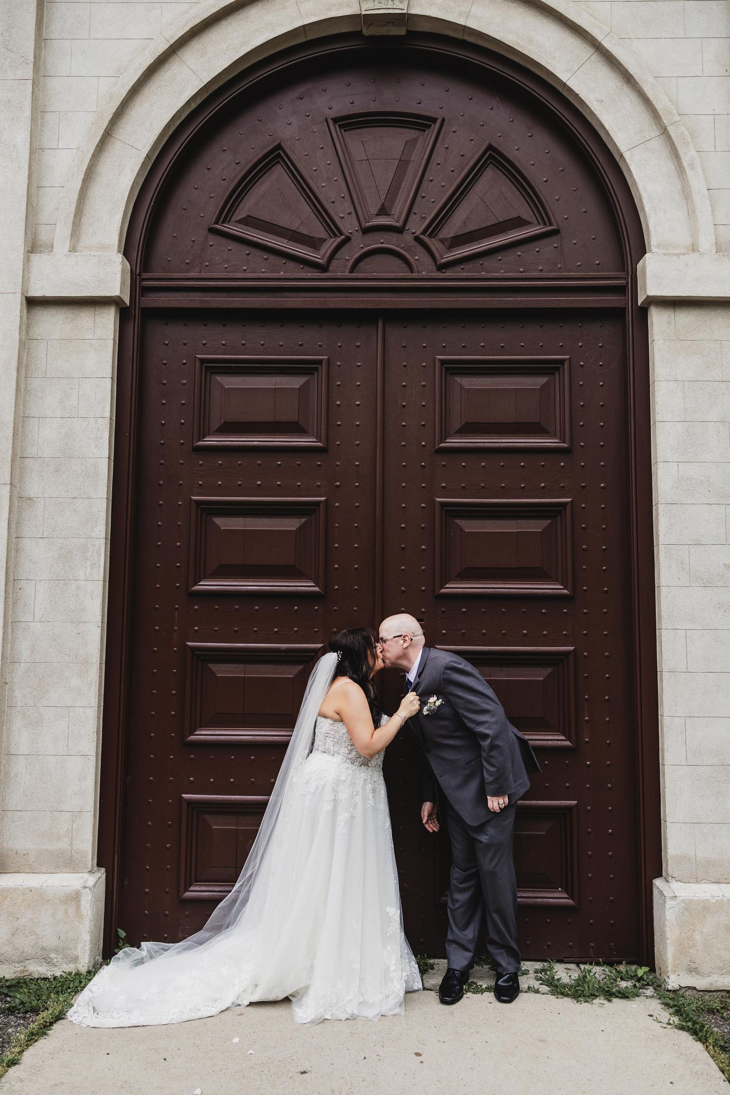 Romantic wedding portrait of couple against large arched wooden door.