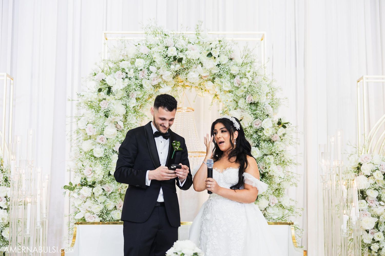 Couple sharing a joyful moment in front of their floral wedding arch backdrop.