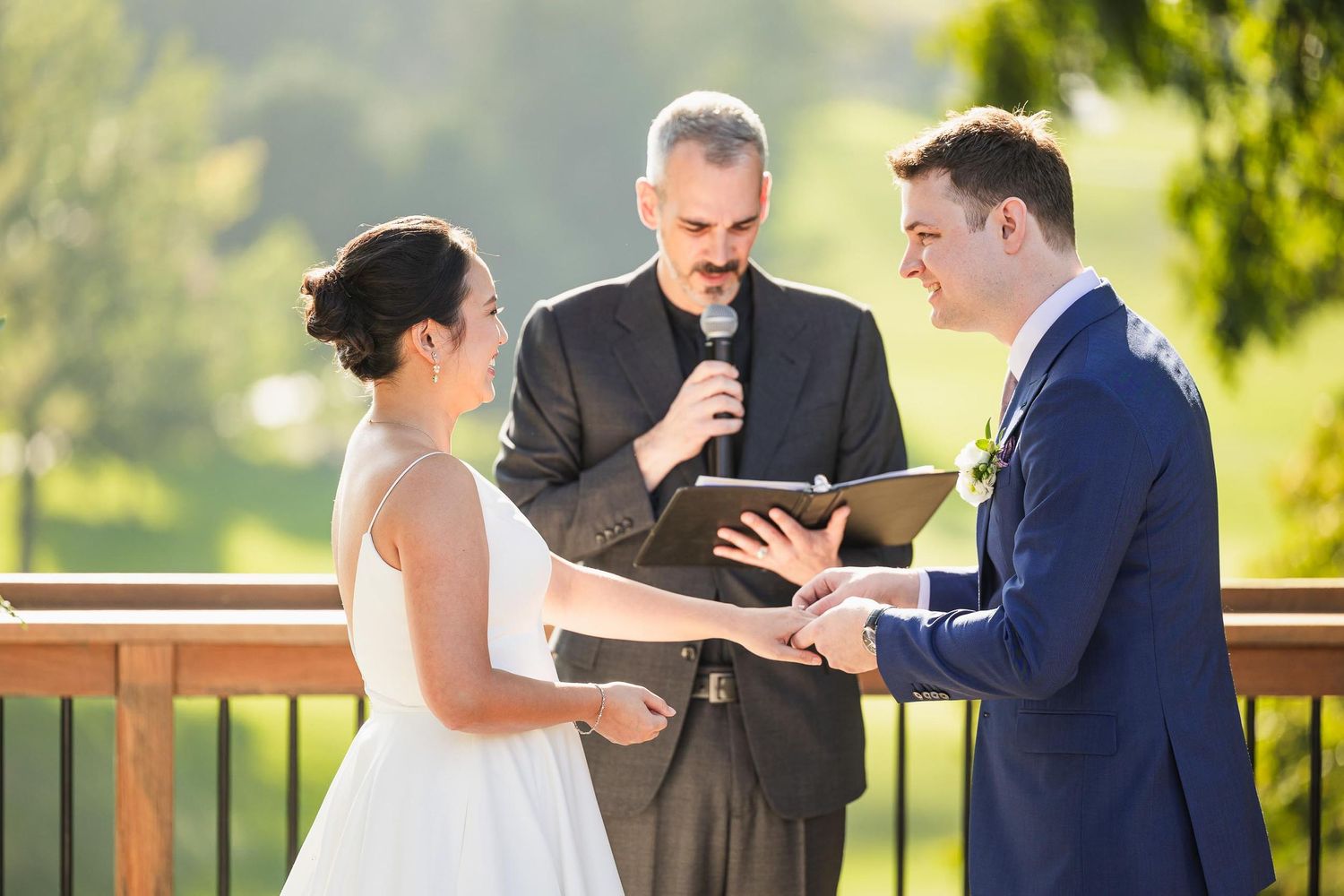 Outdoor wedding ceremony with couple exchanging vows on wooden deck.